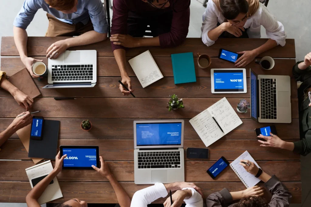 Bovenaanzicht van een team met laptops, tablets en notitieboeken aan een houten tafel