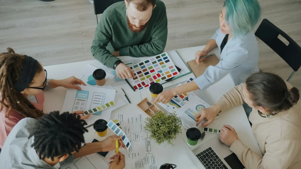 Een team bespreekt kleurstalen en wireframes aan een werktafel